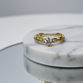 Anillo solitario dorado con una zirconia central en un engaste retorcido o trenzado, sobre una superficie de espejo. Anillo de compromiso o promesa en acero inoxidable baño de oro 18k. Joyería elegante femenina de nudo.